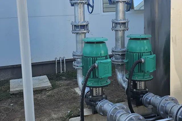 Bombas verdes e tubulações junto à fachada do galpão